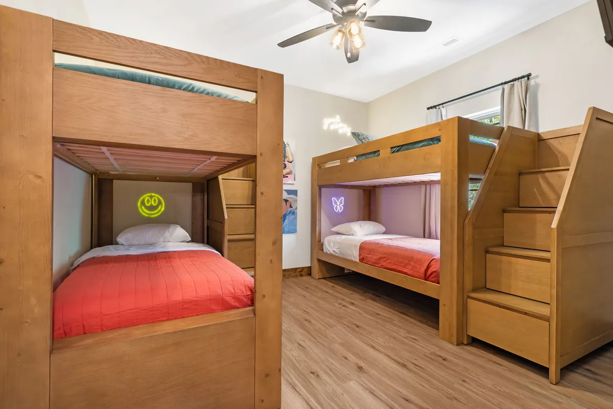 A cheerful bunk room with colorful bedding, built-in bunk beds, playful decorative wall art, and a staircase with integrated storage. The room feels vibrant and welcoming, ideal for children or groups seeking a fun and cozy retreat.