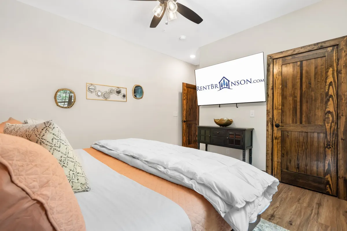 A king bedroom featuring a plush bed with decorative pillows, wall-mounted TV, wooden furniture, and a pair of decorative mirrors. The room glows with soft, natural light, evoking a restful and serene atmosphere ideal for unwinding after a day of adventures.