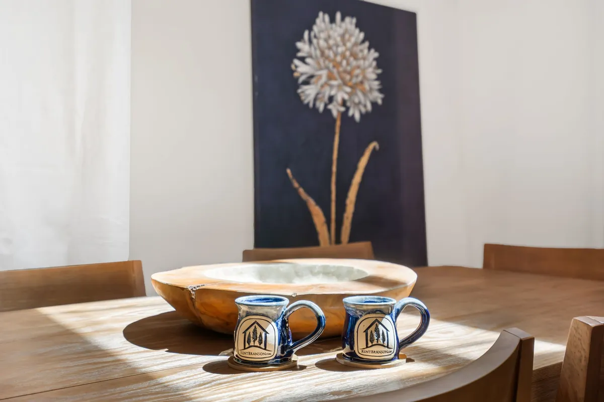 A cozy nook featuring a wooden bowl, ceramic mugs, and attractive artwork on the wall. The scene suggests a coffee bar or breakfast station, creating a sense of morning ritual and comfort.