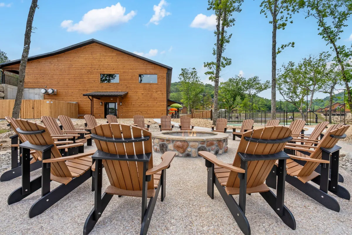 A cozy fire pit surrounded by Adirondack chairs, set amidst trees and adjacent to a wooden building. The setup is perfect for evening gatherings, with a sense of relaxation and togetherness under the stars.
