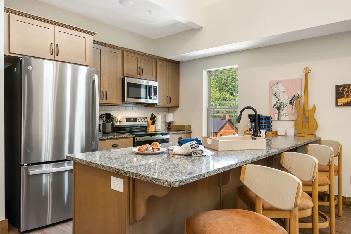 A spacious kitchen featuring a granite countertop, stainless steel appliances, warm wooden cabinetry, a functional kitchen island, and a window bringing in natural light. The layout is open and inviting, ideal for meal prep and casual gathering.