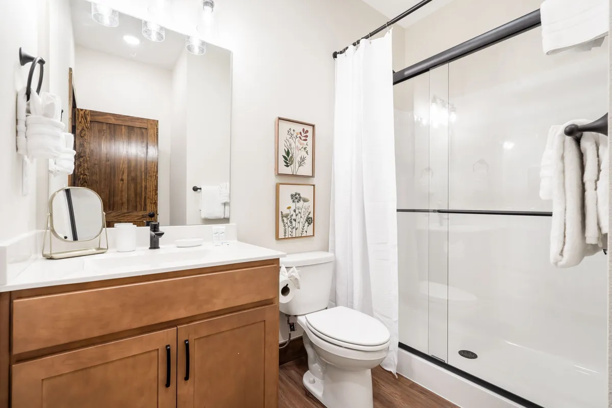 A spa-like ensuite bathroom featuring a vanity with a large mirror, a spacious shower area, and tasteful wall art. The lighting and decor evoke a sense of calm and privacy, perfect for unwinding with a refreshing shower or soothing bath.